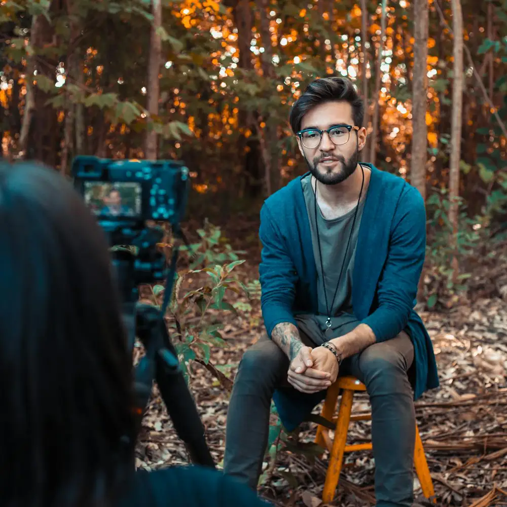 candidature pour un emploi sous forme d'une vidéo. Homme assis sur un tabouret en extérieur dans une forêt en train d'être filmé