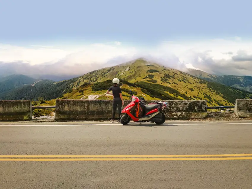 usager d'une moto électrique arrêté sur le bord de la route et admirant un paysage de montagne