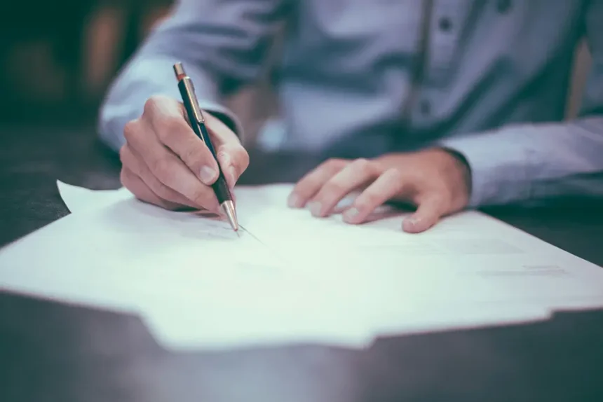 Homme en chemise rédigeant une lettre de motivation au stylo et papier pour accompagner son CV