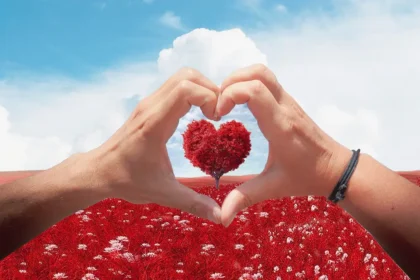 Saint-Valentin : arbre en forme de coeur dans un champs de fleurs rouges, encerclé de deux mains formant un coeur
