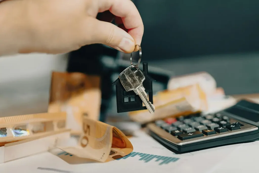 Main tenant des clés de logement avec calculatrice et billets en arrière-plan, illustrant la rentabilité d'un investissement locatif.