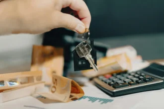 Main tenant des clés de logement avec calculatrice et billets en arrière-plan, illustrant la rentabilité d'un investissement locatif.