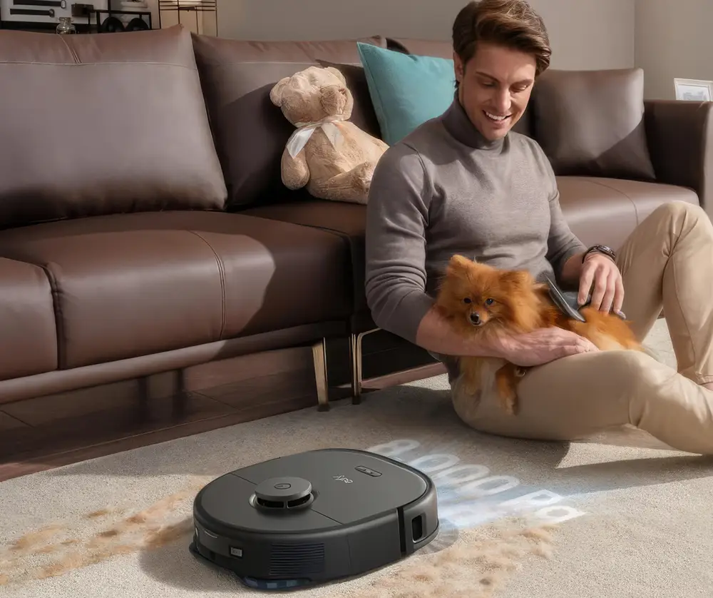 Homme tenant son chien dans les bras, regardant le robot aspirateur nettoyer le tapis du salon des poils d'animaux