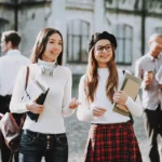 Deux étudiantes en architecture avec livres et cahiers en main au premier plan, et d'autres étudiants en arrière plan