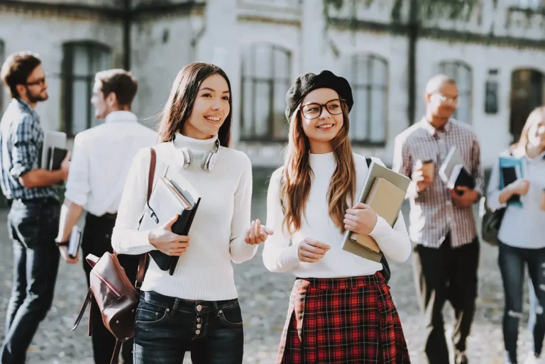 Deux étudiantes en architecture avec livres et cahiers en main au premier plan, et d'autres étudiants en arrière plan