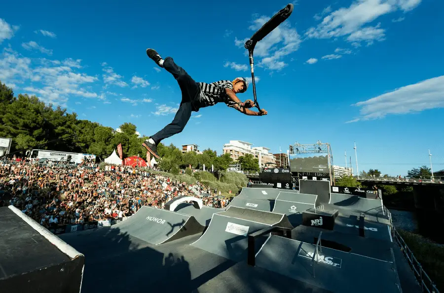 Rider professionnel de trottinette freestyle en plein air spectaculaire lors d'une compétition internationale devant une foule massive au skatepark