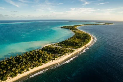 Vue aérienne d'un atoll corallien de Kiribati entre lagon turquoise et océan Pacifique, fine bande de terre bordée de cocotiers