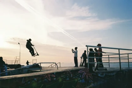 Communauté de riders de trottinette freestyle au skatepark au coucher du soleil, ambiance conviviale avec spectateurs et pratiquants