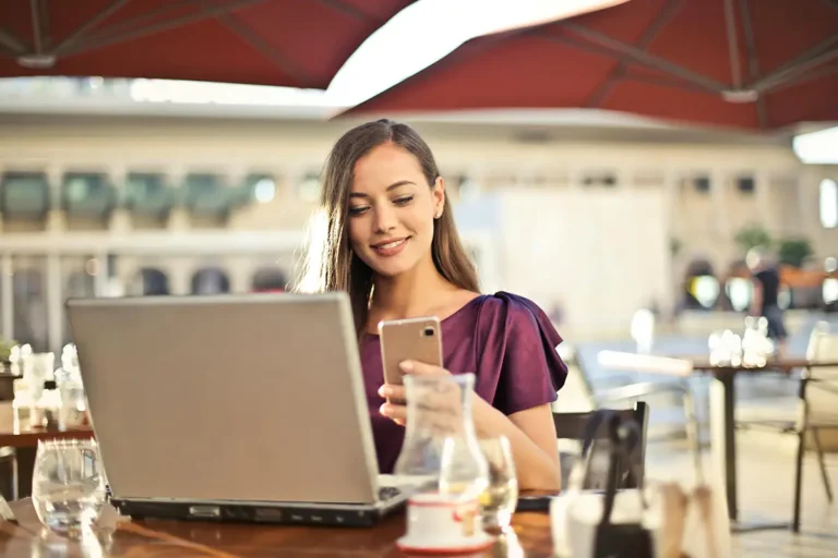Jeune femme travaillant sur un ordinateur portable et smartphone depuis une terrasse de café