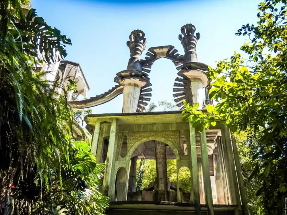 Arche en béton et colonnes sculptées du jardin de sculptures Las Pozas à Xilitla, encadrées par une végétation tropicale luxuriante sous un ciel bleu