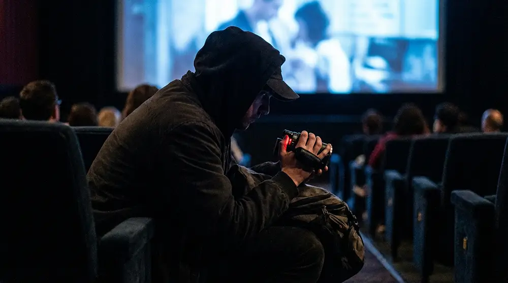 Personne filmant clandestinement un film dans une salle de cinéma avec une caméra dissimulée