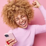 Jeune femme avec son smartphone, heureuse d'avoir téléchargé une application sans problemes