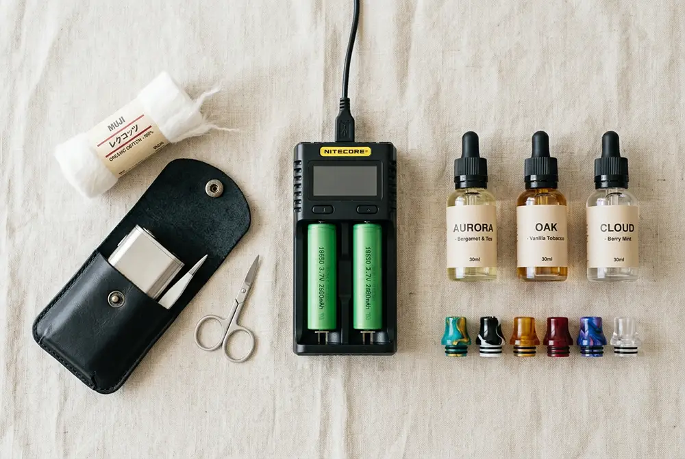 Accessoires de vape : accus 18650, chargeur, drip tips, étui et e-liquides en flat lay