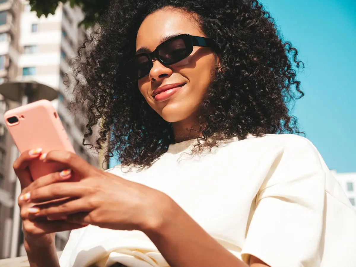 Femme au cheveux bouclés regardant son téléphone en souriant