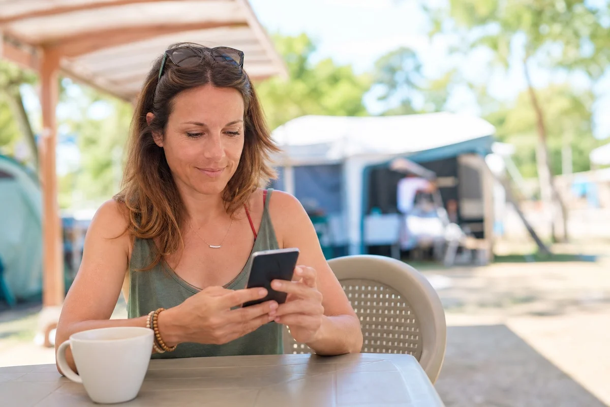Aides vacances VACAF et chèques ANCV pour camping famille Parent consultant son téléphone pour réserver un camping avec aide VACAF CAF et chèques vacances ANCV