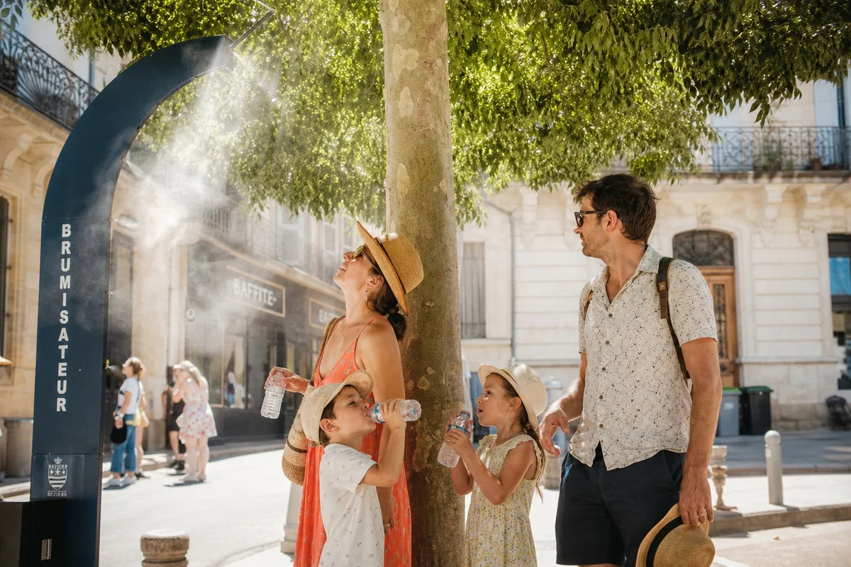 Conseils hydratation et protection chaleur en vacances été 2026 Famille se rafraîchissant avec de l'eau lors d'une visite touristique sous forte chaleur